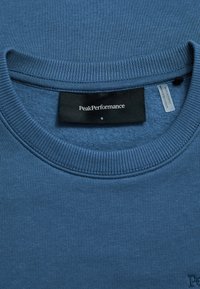 Felpa blu in cotone con collo a girocollo a costine e polsini. Presenta un'etichetta nera con la scritta "PeakPerformance" e la taglia "S".