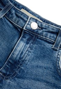 Jean en denim bleu avec une texture délavée, présentant une fermeture à bouton argenté, ainsi qu'une taille et des poches cousues.