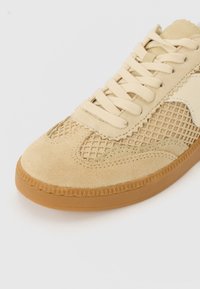 Beige sneaker texturált velúr és hálós felső résszel, lapos fűzőkkel és gumitalppal, amelynek szélén zig-zag minta található.