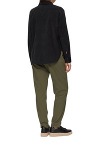 Schwarze Cordhemd mit Knopfleiste und abgerundetem Saum, kombiniert mit olivgrünen tapered Pants und schwarzen Sneakers mit einer klobigen beigen Sohle.