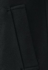 Schwarzer Wollstoff mit einer eleganten, glatten Textur und einer sichtbaren Tasche. Das Design ist minimalistisch mit klaren Linien und ohne zusätzliche Verzierungen.