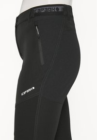 Mustat urheiluhousut, joissa on sileä pinta, vetoketjullinen tasku, erottuva ommel ja logo reidessä. Ominaisuuksia on tiukka malli.