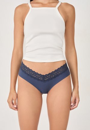 Sous-vêtements bleu marine avec une ceinture en dentelle, fabriqués dans un tissu lisse et au design classique de slip. Le haut est un débardeur blanc à côtes.