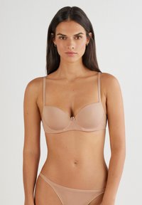 Nude-farvet bh med glatte, polstrede skåle og justerbare stropper. Har en delikat detalje med en sløjfe i midten og en sømløs design for komfort.