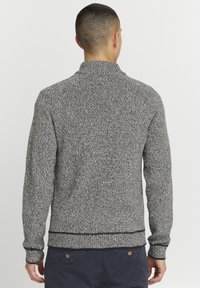 Maglione lavorato a maglia in un motivo a spina di pesce grigio e nero, con maniche lunghe, collo alto e polsini e orlo a coste, realizzato in un materiale morbido e texture.