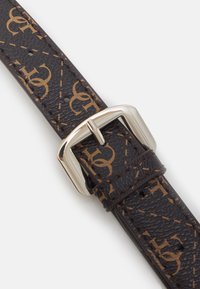 Brązowy skórzany pasek do zegarka z monogramem, teksturowaną powierzchnią i srebrnym metalowym zapięciem dla bezpiecznego mocowania.