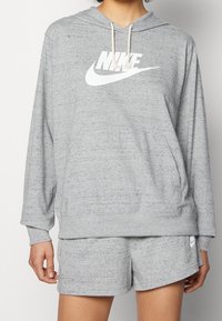 Gray hoodie with a textured finish, featuring a large white Nike logo on the front. Paired with matching gray shorts.