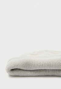 Sykla beanie i lys grå, med vrangbord og teksturert mønster. Materialet ser mykt og elastisk ut.