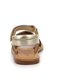 Sandalia de cuero marrón con correas metálicas doradas, diseño de punta abierta, cierre ajustable en el tobillo y plantilla acolchada con logotipo impreso.