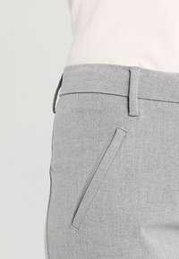 Šedé upravené kalhoty s hladkou texturou, slim fit a jedním šikmým postranním kapsovým detailem. Čistý design pásku bez viditelného kovového zapínání.
