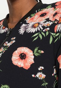 Kwiatowa kurtka bomberka na czarnym tle, z dużymi koralowymi i białymi kwiatami. Zapięcie na zamek błyskawiczny i prążkowany kołnierz. Miękka w dotyku.