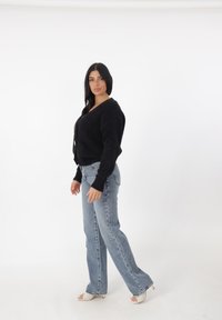 Cárdigan de punto negro corto con mangas largas y botones, combinado con unos pantalones vaqueros de pierna ancha de talle alto en azul claro y tacones abiertos blancos.