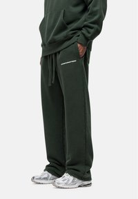 Donkergroene sweatpants met een ontspannen pasvorm, voorzien van een trekkoord in de taille en de tekst "GOODFORNOTHING" in wit aan de linkerzijde.