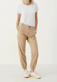 Beige elastiska byxor med smal passform, kombinerat med en åtsittande vit t-shirt. Bärs med vita och gula sneakers.