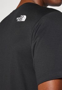 Μαύρο κοντομάνικο μπλουζάκι φτιαγμένο από υφασμάτινη υφή, με άσπρο λογότυπο της The North Face στο επάνω μέρος της πλάτης. Απλός, κομμένος σχεδιασμός.