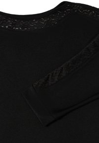 Pull noir avec un panneau en dentelle noire texturée et transparente le long du col et des manches ; tissu doux, col rond, poignets ajustés.