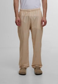 Lette, stripete loungebukser i beige og krem; elastisk midje; avslappet passform; glatt tekstur; ankellang; kombinert med brune sko.