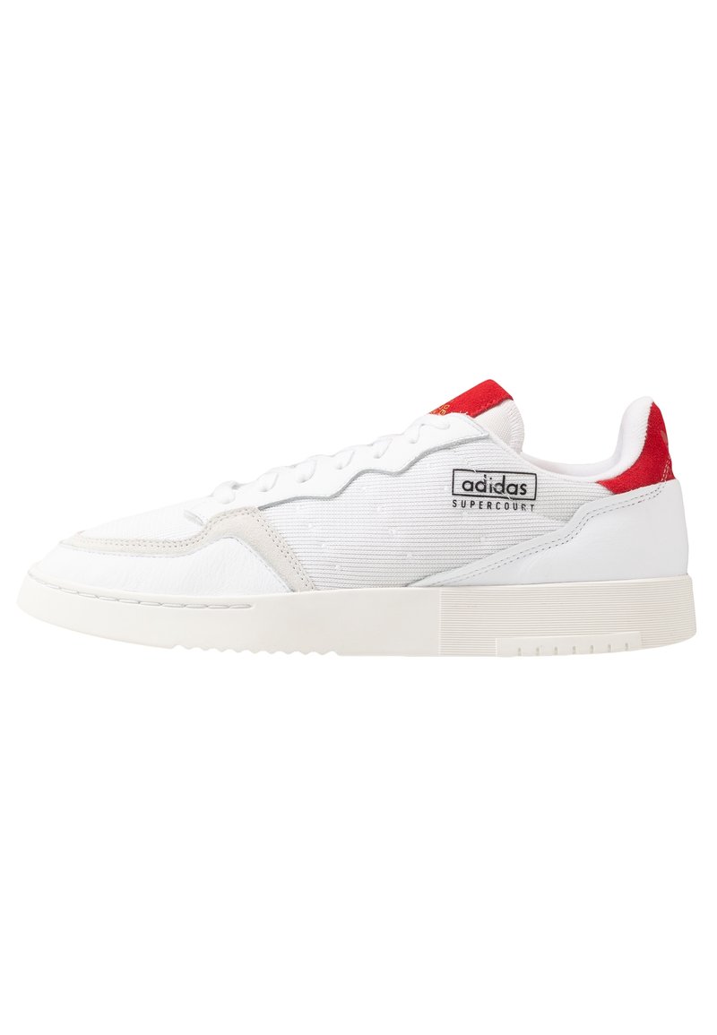 White Adidas Supercourt sneaker with red accents on heel and tongue, textured sole, and stitched panel details.