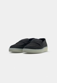 Scarpe in suede nero con punta arrotondata, caratterizzate da un design di fasce sovrapposte e una suola in gomma leggera a contrasto.
