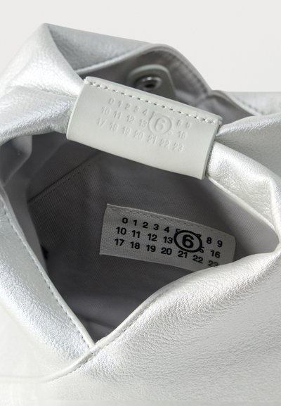 Εσωτερική άποψη ασημένιας δερμάτινης τσάντας που δείχνει μια ραμμένη ετικέτα και μια ανάγλυφη ετικέτα με αριθμούς από 0 έως 23, με τον αριθμό 6 κυκλωμένο.