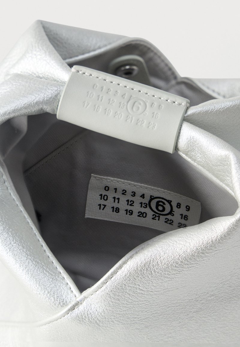 Vue intérieure d'un sac en cuir argenté montrant une étiquette cousue et une languette embossée avec les chiffres de 0 à 23, le numéro 6 étant entouré.