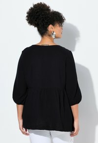 Black, textured blouse with a loose, gathered bottom and three-quarter balloon sleeves. Back features a wide neckline and smooth fabric.