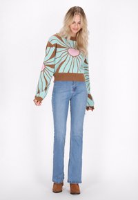 Maglione a maglia con un motivo a raggi di sole turchese e marrone, arricchito da dettagli rosa. Abbinato a jeans a zampa d'elefante blu chiaro e stivaletti marroni.