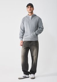 Grå hettegenser med glidelås og løs passform. Bæres med falmede sorte jeans og hvite joggesko med svarte striper. Enkel og uformell design.