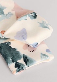 Tela suave con estampado de colores pastel claros, con diseños florales abstractos en verde, rosa y azul. Texturizada y doblada.