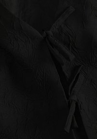 Juodas tekstūruotas audinys su susiraukšlėjusiu paviršiumi. Yra užrišama uždanga su dviem kilpomis. Lygus paviršius su švelniu, matinio tipo apdaila.