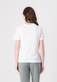 White cotton t-shirt with short sleeves, crew neckline, and a smooth texture, displayed from the back. Paired with gray sweatpants.