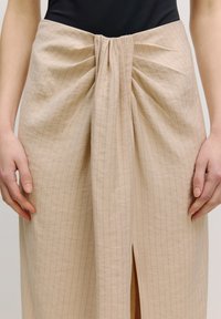 Beige rok met verticale strepen, voorzien van een verzamelde knoopdetail bij de taille en een split aan de voorkant. Soepele stof, getailleerde silhouet.
