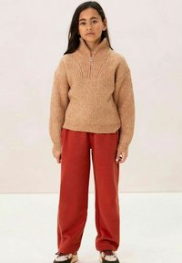 Hellbrauner, gerippter Strickpullover mit einem halben Reißverschluss am Kragen. Kombiniert mit locker sitzenden, roten Hose. Sneaker mit einem mehrfarbigen Design.