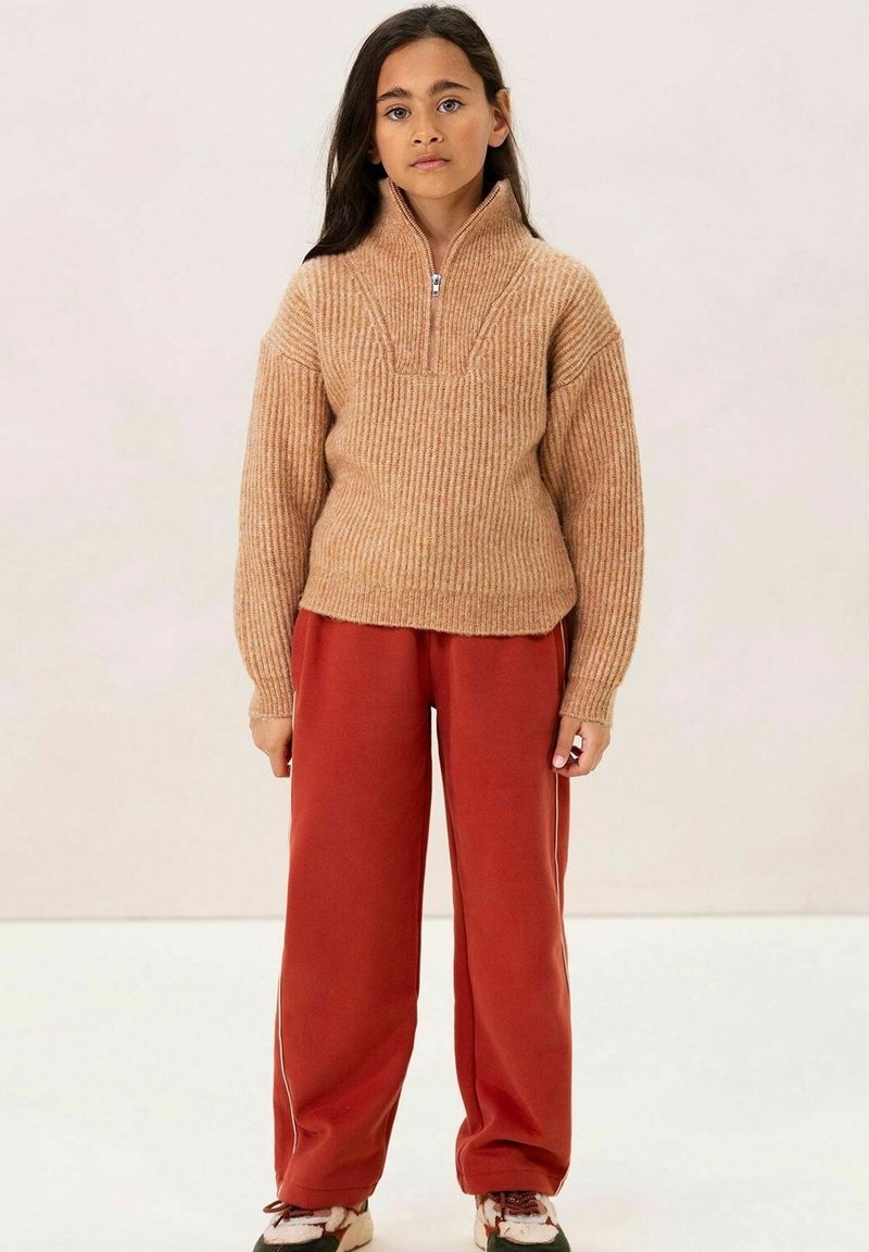 Hellbrauner, gerippter Strickpullover mit einem halben Reißverschluss am Kragen. Kombiniert mit locker sitzenden, roten Hose. Sneaker mit einem mehrfarbigen Design.