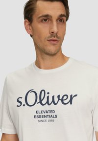 Witte katoen t-shirt met een ronde halslijn, voorzien van marineblauwe bedrukte tekst: "s.Oliver ELEVATED ESSENTIALS SINCE 1969."