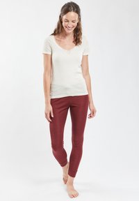 Top corto a maniche corte di un beige chiaro con bordo in pizzo e leggings rossi aderenti, entrambi in un tessuto liscio ed elastico. Design minimalista con colori neutri.