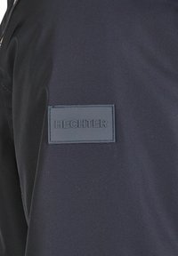 Veste marine avec une texture lisse, des coutures discrètes et une étiquette en caoutchouc rectangulaire embossée avec "HECHTER."