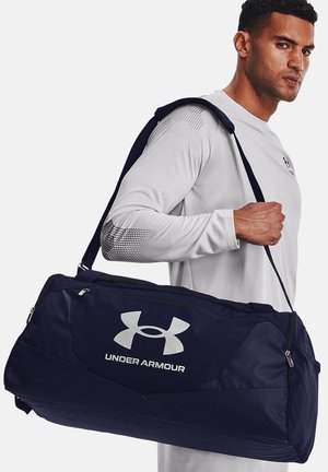 Marine duffel tas gemaakt van duurzaam materiaal, met een zilveren logo, dikke schouderriem en ritsen voor een veilige sluiting.