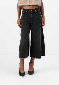 Crne traperice culottes sa  širokim nogavicama, sirovim rubom i suptilnim izbljeđivanjem. U paru s crnim cipelama s oštrim vrhom i skraćenom krznom jaknom.