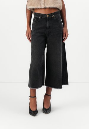 Culotte in denim nero con taglio ampio, orlo grezzo e un leggero effetto sbiadito. Abbinati a décolleté nere a punta e un top in pelliccia corto.