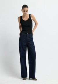 Czarny prążkowany top na ramiączkach połączony z ciemnoniebieskimi spodniami o szerokich nogawkach. Wydłużona sylwetka z gładkimi fakturami i minimalnymi akcentami sprzętowymi.