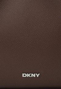 Brązowa torebka skórzana o fakturze z metalowym logo "DKNY" na dole, z gładką powierzchnią i subtelnym wzorem ziarna.
