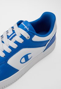 Blue and white athletic shoes with a smooth synthetic upper, textured panels, contrasting blue accents, and classic white laces.