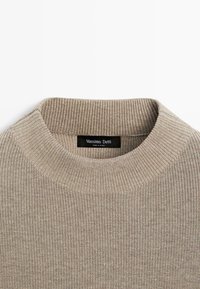 Pull en maille côtelée beige avec un col rond et une étiquette noire indiquant "Massimo Dutti Made in China" à l’intérieur du col.