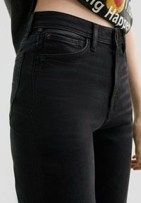 Jeans de mezclilla negra con cintura alta, que cuentan con cinco bolsillos, un ligero desvanecimiento y un ajuste ceñido a lo largo de las piernas, fabricados con material elástico.