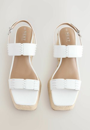 Witte wig-sandalen met twee brede banden, met een geweven textuur, vierkante neuzen en een gevlochten jute tussenzool. Accent van een zilveren gesp.