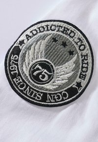Black and white circular embroidered patch featuring "Addicted to Ride" text, wings, stars, and the number "75" with a textured background.