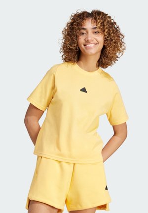 Camiseta de algodón amarilla con un corte relajado, mangas cortas y un logo triangular negro en el centro. Combinada con pantalones cortos amarillos a juego.