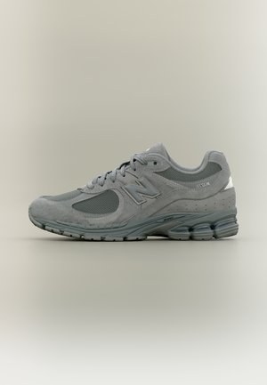 Baskets New Balance 2002R grises avec tige en mesh et en daim, semelle rembourrée et logo sur le côté et la languette, présentées de profil sur un fond neutre.