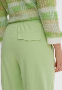 Světle zelené kalhoty s elastickým pasem mají zadní kapsu a hladkou, měkkou texturu. Materiál má mírný lesk a elegantní střih.